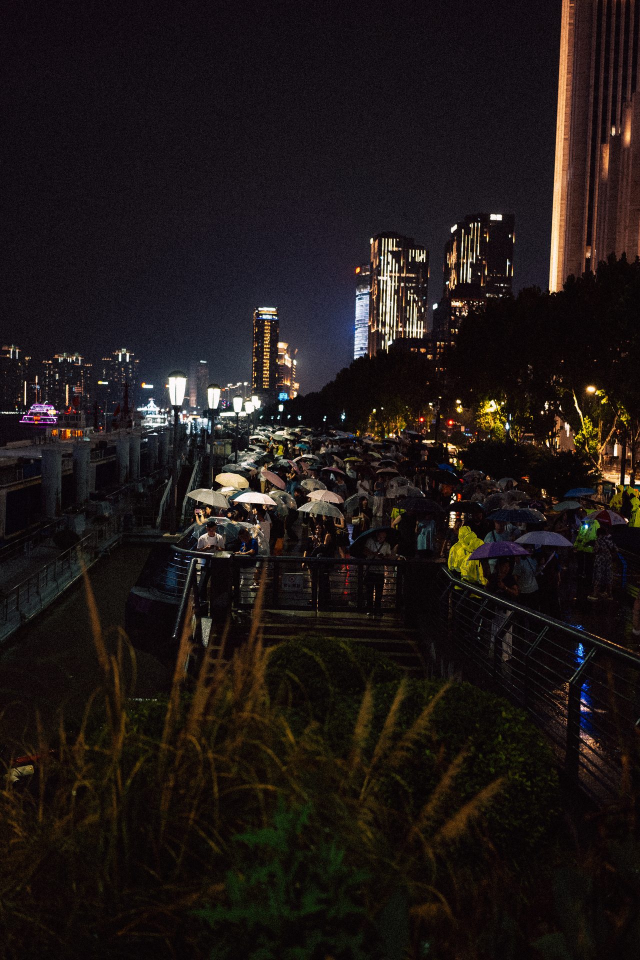 Crowd with umbrellas on a riverside promenade at night