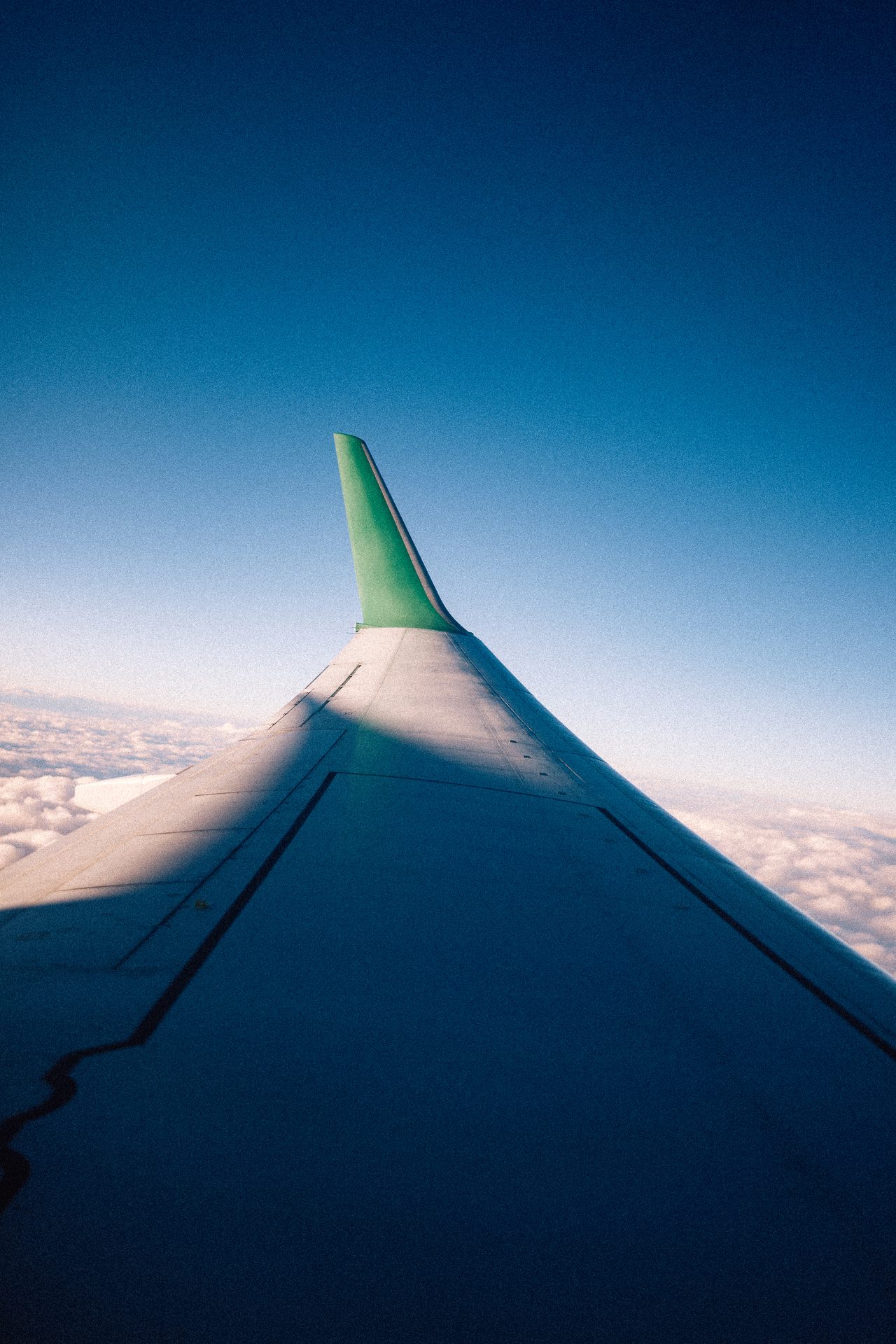 Airplane wing above a sea of clouds under a blue sky