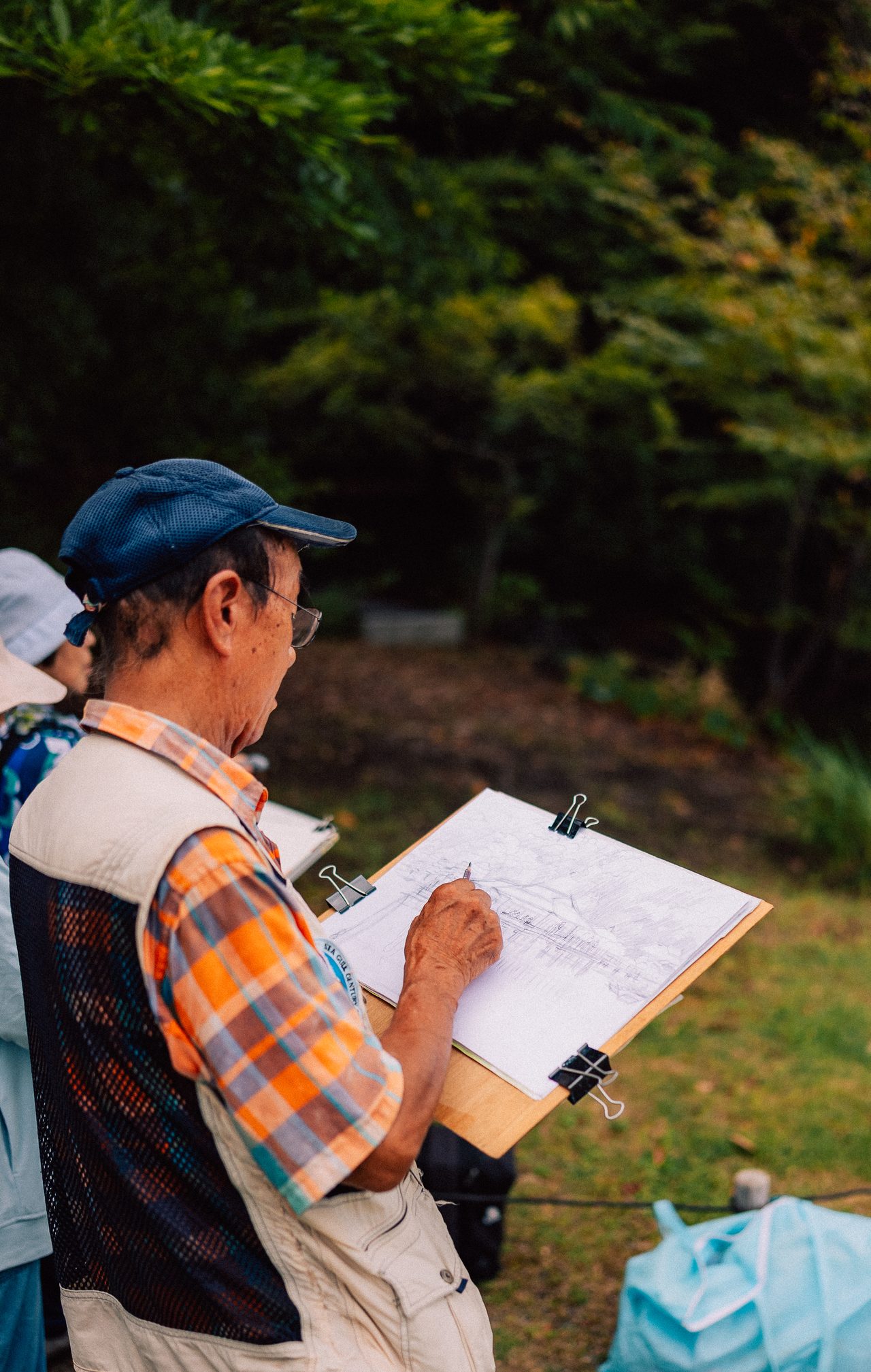 Man sketching a landscape on a clipboard in a park