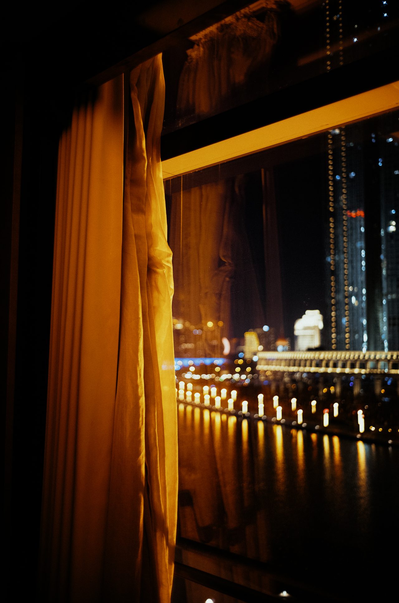 Warm hotel curtain framing a nighttime river skyline