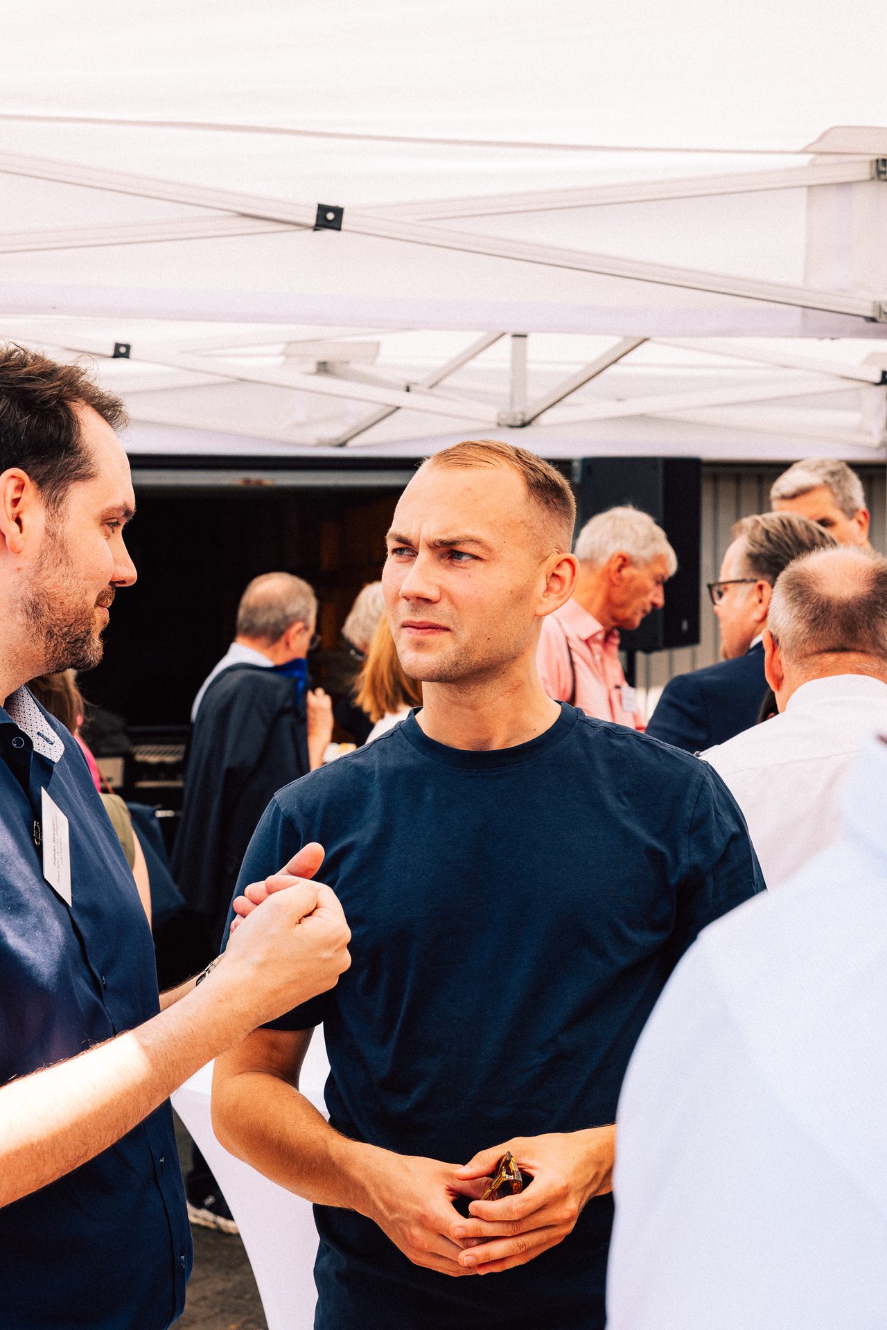Two men talking beneath a white pavilion
