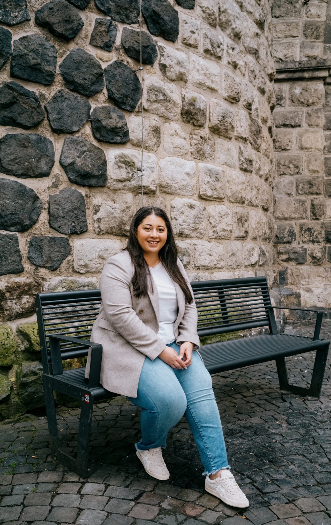 Sanae Abdi seated in front of a historic stone wall in Cologne